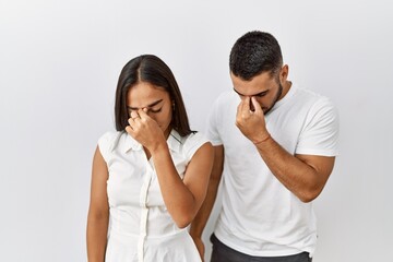 Young interracial couple standing together in love over isolated background tired rubbing nose and eyes feeling fatigue and headache. stress and frustration concept.