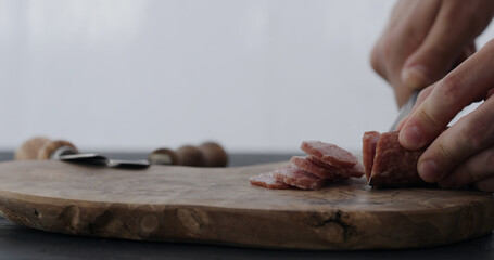 man slicing salami on olive board