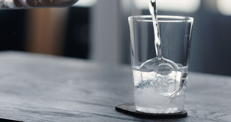 pour tonic water over clear ice ball in tumbler glass on black oak table