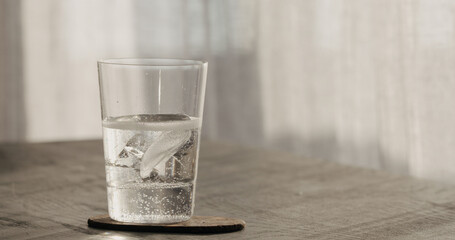 clear ice cube in tumbler glass with tonic on black oak table
