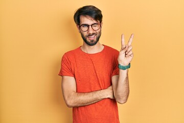 Young hispanic man wearing casual clothes and glasses smiling with happy face winking at the camera...