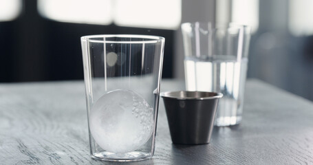 put clear ice ball in tumbler glass on black oak table