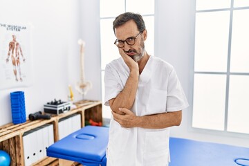 Middle age man with beard working at pain recovery clinic thinking looking tired and bored with depression problems with crossed arms.