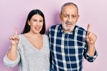 Hispanic father and daughter wearing casual clothes with a big smile on face, pointing with hand finger to the side looking at the camera.