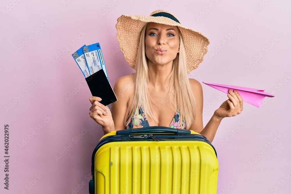 Canvas Prints young blonde woman wearing bikini holding passport and paper plane looking at the camera blowing a k