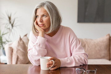 Sad pensive middle age woman looking down depressed sitting on the sofa