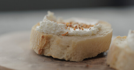 spices on cream cheese on fresh baguette slice on olive board closeup