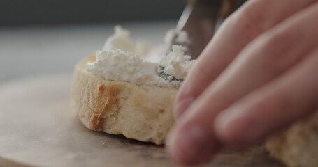 spread cream cheese on fresh baguette slice on olive board closeup