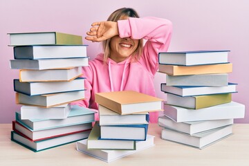 Young caucasian woman sitting on the table with books smiling cheerful playing peek a boo with hands showing face. surprised and exited