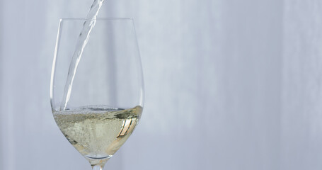 white wine pour into wineglass with curtains on background
