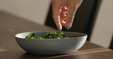 put kale in blue bowl on walnut table making salad