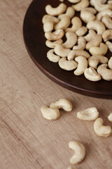 Tasty cashew nuts on a wooden plate on a wooden table, side view. Space for text