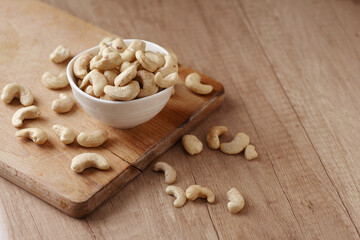 Tasty cashew nuts in bowl on a wooden cutting board on wooden table, side view. Space for text