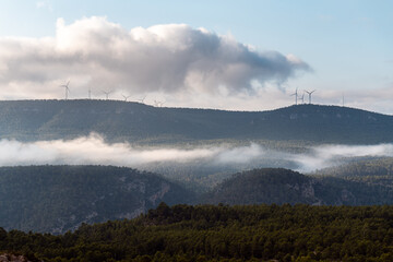 Mountainous landscape, with large pine forests partially covered in mist, on a cool autumn morning. 