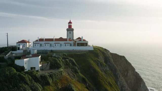 Aerial view of a lighthouse surrounded with rugged coastline. Rocky cliffs overlooking the roaring Atlantic Ocean seen from above. Europe, Portugal, Sintra, Cabo da Roca. High quality 4k footage