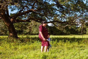 Pregnant mother and toddler daughter spending time outdoors. Happy maternity scene of mother and toddler expecting a second child.