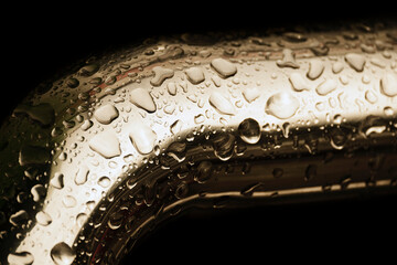 Abstract background. Yellow metal pipe covered water droplets. Raindrops on bend of metal pipe isolated on black. Shiny water droplets on surface of metal. Rain water drop on stainless rail.