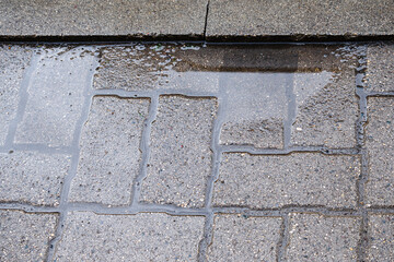 A puddle after rain on an uneven tile surface. Improperly laid gray paving slabs. Errors in paving...