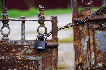 Rusty old padlock on metal gate closeup. Dirty lock on closed. lock on chains. Protection, security and safety concept. Private property entrance. old rusty iron texture.