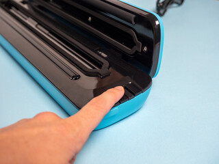 close-up of a woman's hand pressing the button of a blue vacuum packer. Concept of devices for food preservation and storage