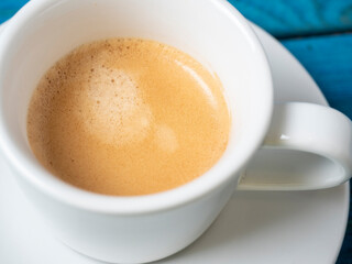 close-up of fragrant and invigorating coffee in a white cup on a blue wooden background.