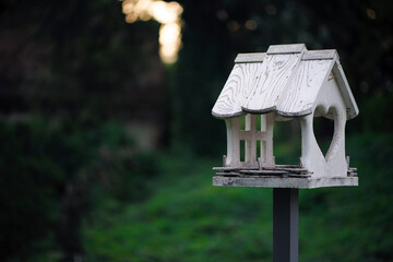 bird feeder in the autumn park. A closeup photo of a white wooden birdhouse in the park. Bird feeders. Bird house. Selective focus, bokeh, blurred yellow-green background. Copy space