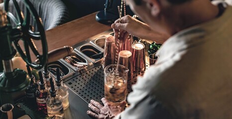 An expert bartender mixing a cocktail in a glass mixer with a long spoon, standing behind the...