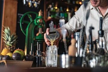 A professional bartender pouring a cocktail in a glass from a shaker and mixer, view of a barman working in a bar.