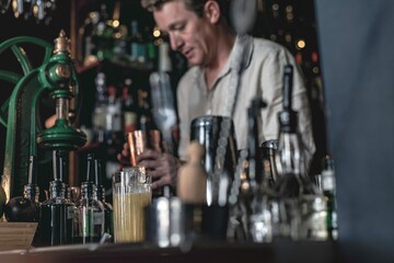 A professional bartender working in a fancy cocktail bar serving a colourful tropical drink while standing behind the counter in a night club.