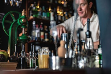 A professional bartender working in a fancy cocktail bar serving a colourful tropical drink while standing behind the counter in a night club.