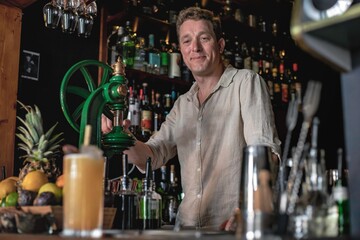 A professional bartender working in a fancy cocktail bar serving a colourful tropical drink while standing behind the counter in a night club.