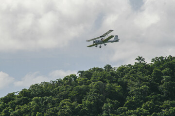 Light aircraft flying over the trees on a cloudy day
