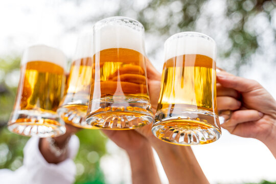 Group of people enjoying and toasting a beer outdoors - Close-up on four pint of beer