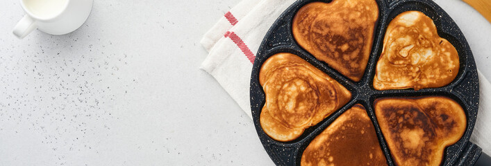Pancakes in shape of breakfast hearts with chocolate sauce in gray ceramic plate, cup of coffee on gray concrete background. Table setting for Valentines Day breakfast. Top view copy space. Banner.