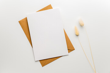Greeting, wedding or congratulations stationery mockup. Blank greeting card on craft envelope and two blades of bunnytail or hare's-tail grass (Lagurus ovatus). Table top view, flat lay, copy space.