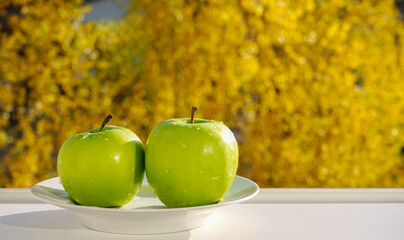 Green apple on a yellow background, close up. Still life on the window opposite the autumn forest.