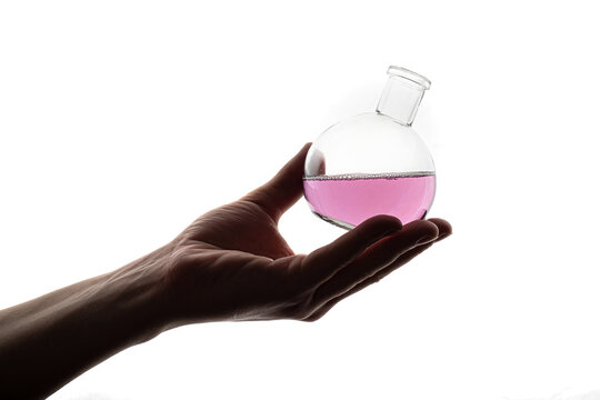 A round flask filled with purple liquid lies on a hand on a white background