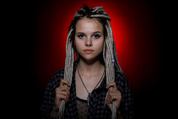 Portrait of a young woman with dreadlocks and piercings in colored lighting. Modern hairstyle style.