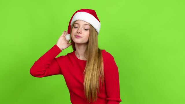 Teenager girl with christmas hat listening to something by putting hand on the ear over isolated background. Green screen chroma key