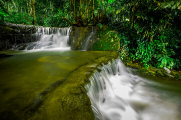 The natural background of waterfalls that blur the flow of water, with various tree species surrounded and boulders of various sizes, the beauty of the ecosystem and the jungles of forests.
