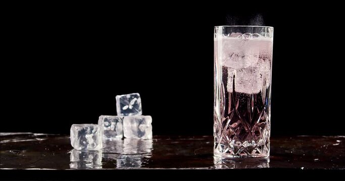 Glass of cold sparkling drink with ice. Slow motion, copy space, black background. Hard seltzer, sparkling water, gin tonic, soft drink.
