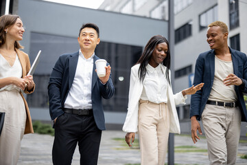 Multiracial businessteam walking and talking on city street. Concept of modern successful business people. Idea of business cooperation. Remote and freelance work. Joyful people wearing formal wear