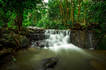 Fototapeta premium The natural background of waterfalls that blur the flow of water, with various tree species surrounded and boulders of various sizes, the beauty of the ecosystem and the jungles of forests.