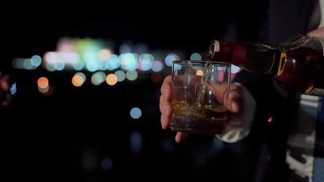 Unrecognizable businessman pouring glass with alcohol closeup. Business meeting of group people at night city view outdoors