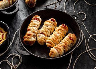 Mummy dogs made of sausages and puff pastry on a black background, close up view. Halloween funny food idea for  party.  