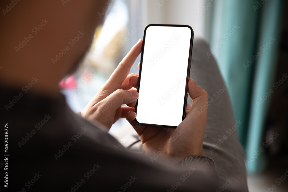 Wall mural man using smartphone blank screen frameless modern design while sitting on the chair in home interio