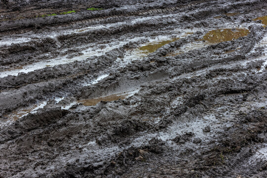 Black wet dirt road with puddles of dirty water at day light