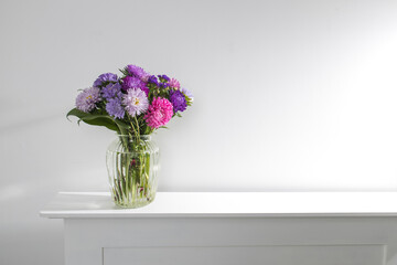 bouquet of colorful asters are on a white dresser