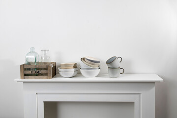 kitchen utensils, cups of different sizes and shades, bowls, bottles, storage items, are on a white dresser.