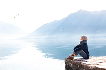 Young woman relaxing at winter sea beach. Traveler resting by blue mountain - obrazy, fototapety, plakaty
